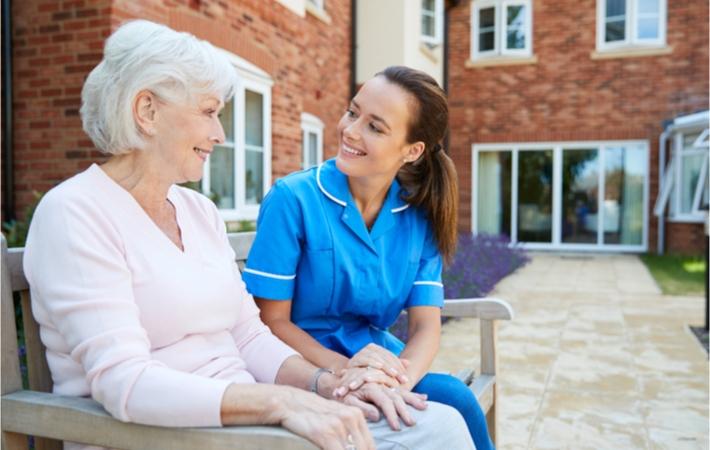 Senior Woman Sitting On a Bench And Talking With a Nurse In a Personal Care Home