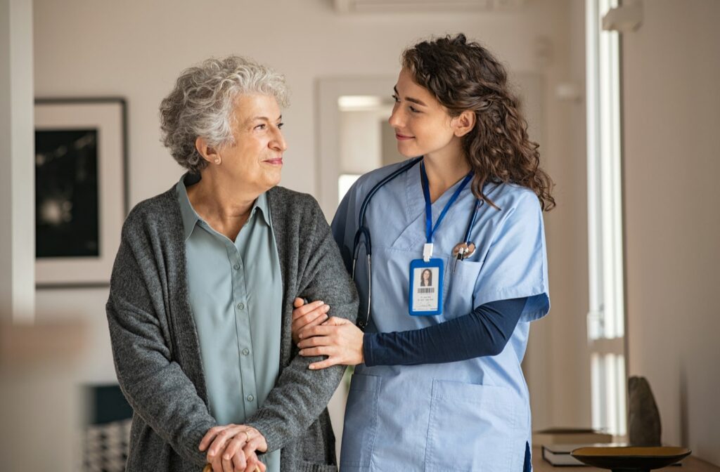 A young nurse linking arms with a female senior at a retirement home and helping her walk down the hall