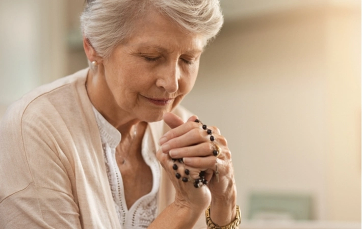 An older woman praying with rosary beads in her hands.