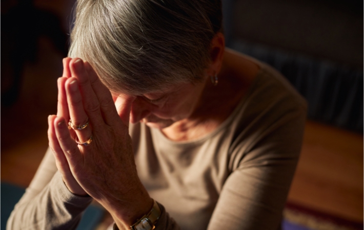 A woman praying with her hands together at her head while bowing.