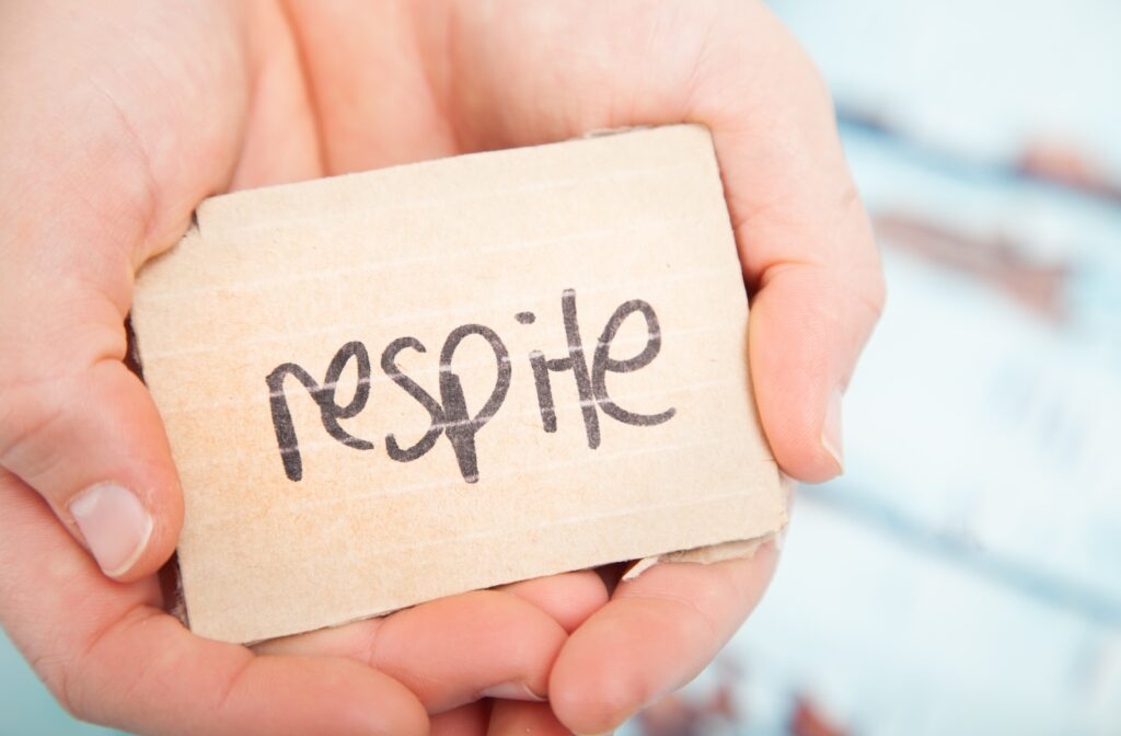 Two hands holding a block with the word respite written in black marker.