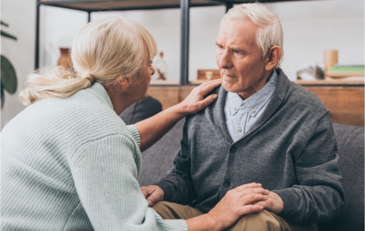 A home care worker checks on an elder male resident sitting on the couch.