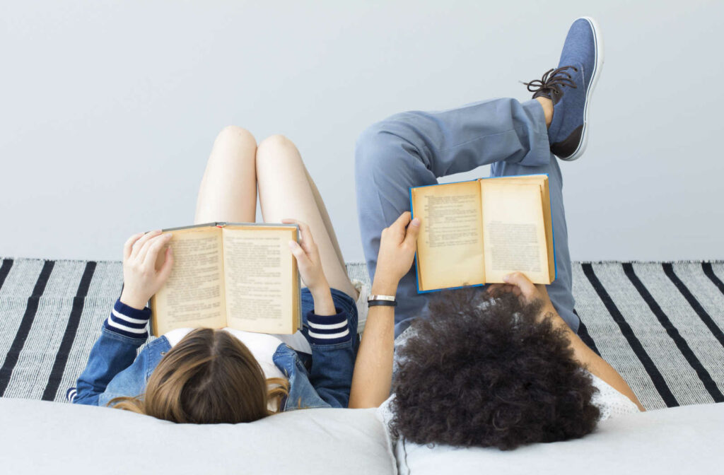 A boy and girl reading books while laying on the ground.