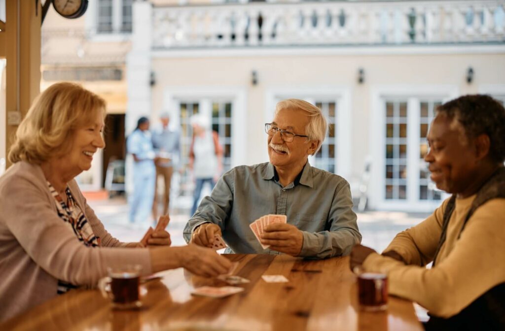 A trio of senior friends play cards together at an outdoor table at an independent living community