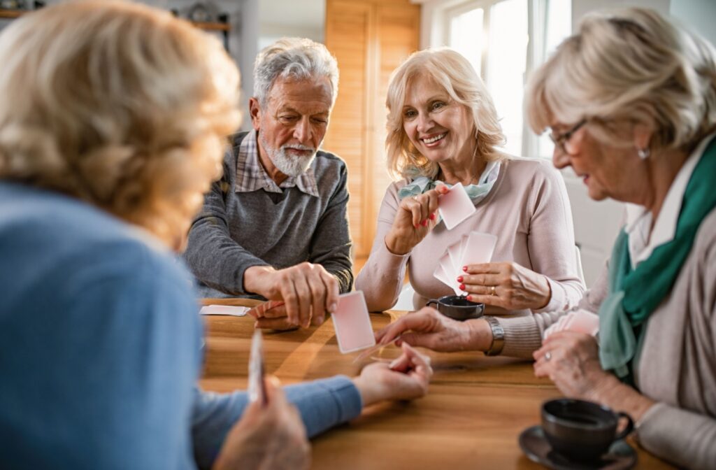 4 seniors play a card game at a wooden table in a well-lit living space.