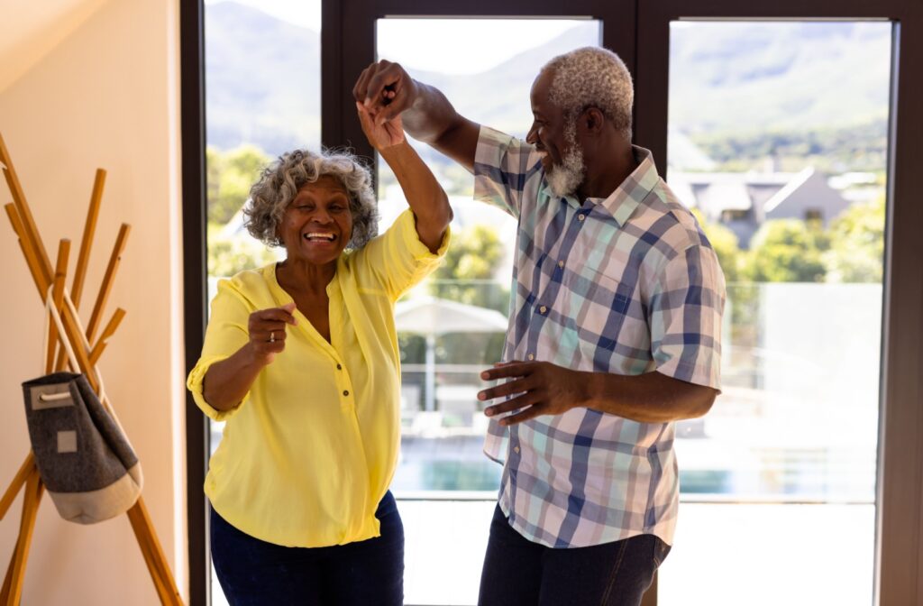 A senior couple cheerfully dances together in a brightly lit home