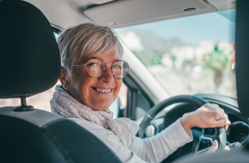 A smiling older adult checks over their shoulder while driving.