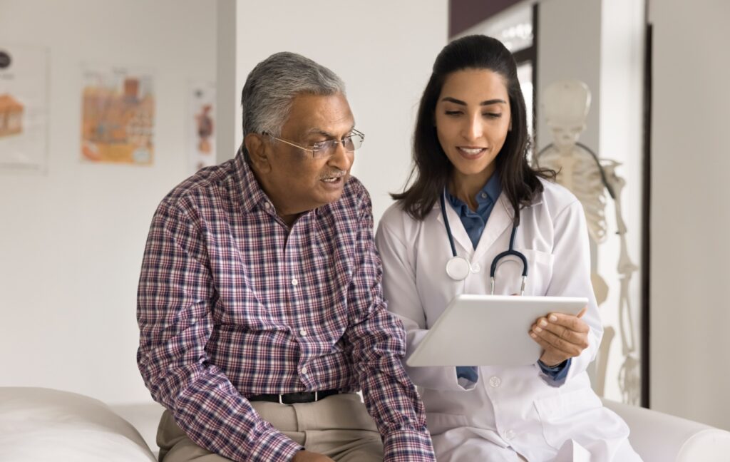 A doctor sits next to their senior patient and carefully explains the results of the patient's dementia testing to the patient.