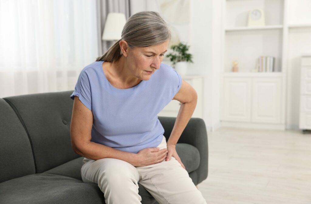 An older adult wincing and rubbing their hip while sitting on their couch in senior living.