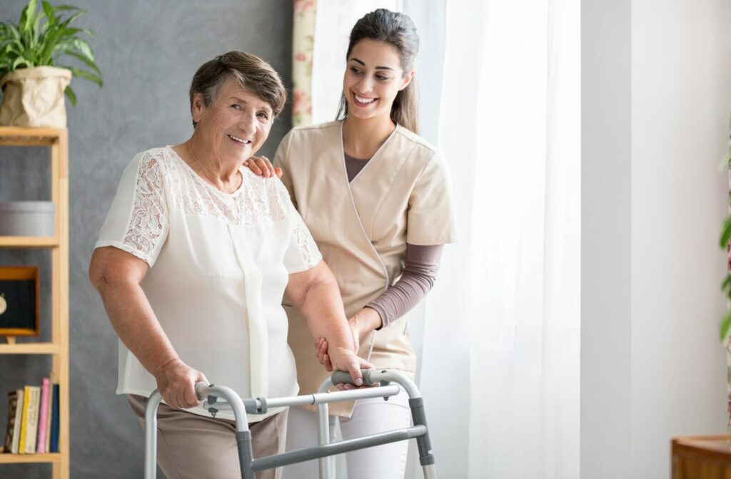 A caregiver smiling while supporting a resident as they use a walker during occupational therapy.