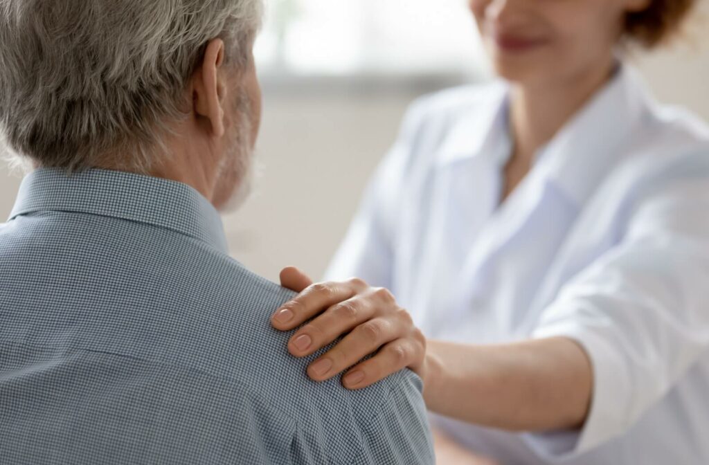 A caregiver in memory care gently touches a resident's shoulders to reassure them about their recent cognitive changes