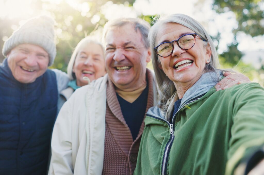 A group of senior friends smile and laugh as they take a selfie.