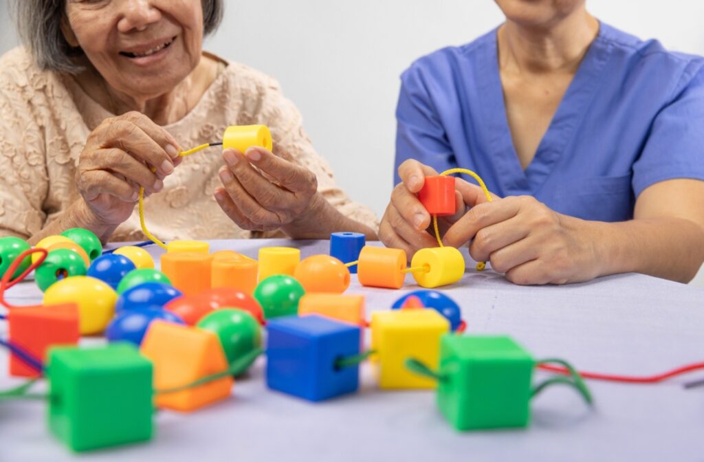 A memory care resident participates in a cognitive puzzle with the help of a caregiver in a senior living community.
